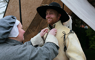 A woman Civil War re-enactor helps a man in seventeenth century clothes to dress